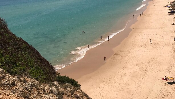 A beach with clear turquoise water, sandy shore, and rocky cliffs.