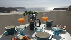 A table set with breakfast items including toast, fruit, and beverages, overlooking a beach and ocean.