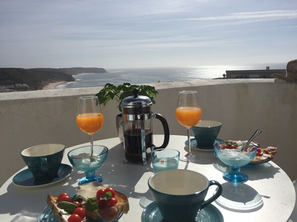 A table set with breakfast items including toast, fruit, and beverages, overlooking a beach and ocean.