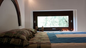 Ein Schlafzimmer mit großem Fenster, einem Bett mit floraler Bettwäsche, einem Nachttisch mit Kerzen und einer an der Wand befestigten Uhr.