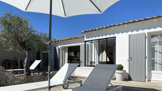 Een houten terras met twee witte ligstoelen en een grote parasol.