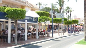 Een terras met tafels en stoelen, palmbomen en een gebouw met een bord.