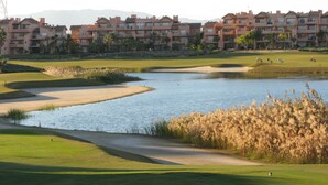 Een golfbaan met een waterhindernis, zandbakken en hoogbouw op de achtergrond.
