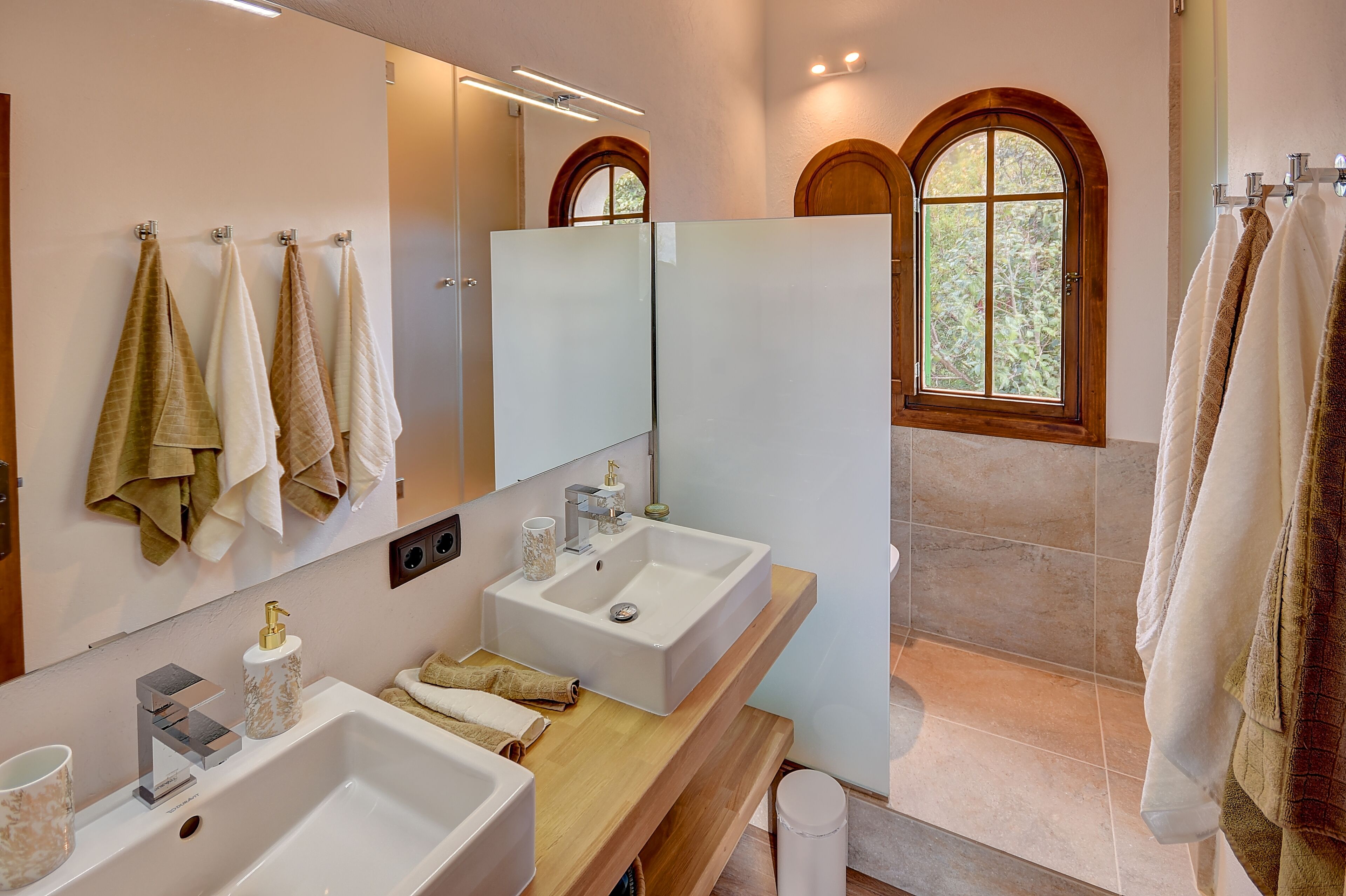 Een moderne badkamer met twee wastafels, een grote spiegel en een raam met een rondboogvormig ontwerp.