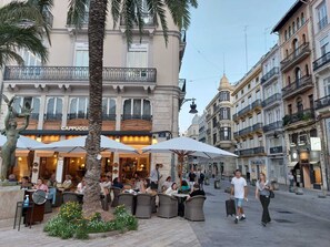 Un café con terraza al aire libre, palmeras y un edificio con el letrero 'Cappuccino'.