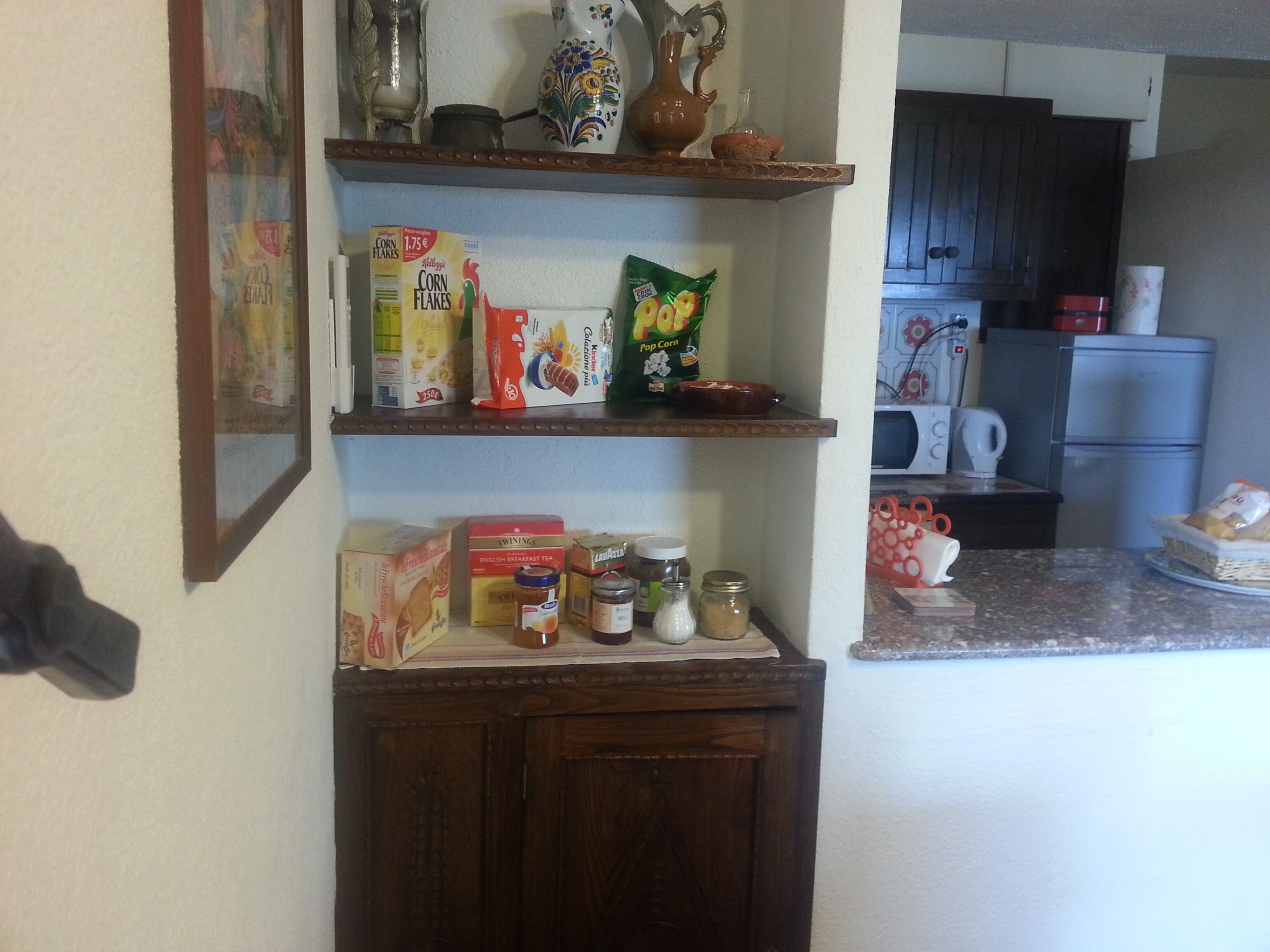 Una cocina con estantes que contienen cajas de cereales, frascos y un microondas.