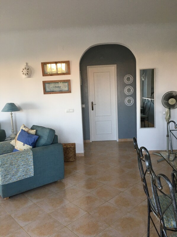 Un salón con un sofá, una mesa y una silla. Hay una puerta que da a otra habitación.