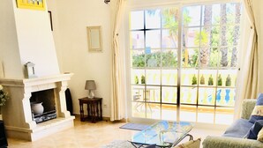 Una sala de estar con chimenea, un sofá, una mesa de comedor y vistas al exterior a través de amplios ventanales.