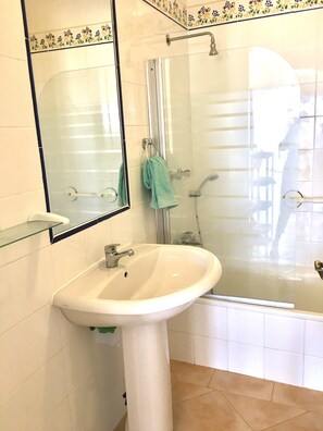 A bathroom with a glass shower enclosure, a white sink, and a mirror with a decorative tile border. - Secluded Lovely 2 Bedroom Ground Floor Apartment  with WiFI  Pool and Garden  (Praia da Luz)