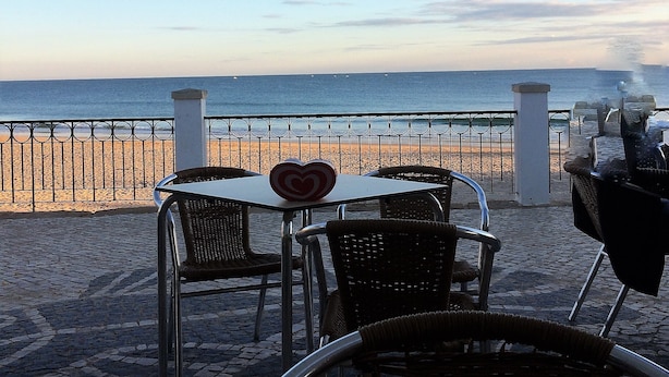 Un patio frente al mar con mesas y sillas, con vista a la playa y al océano.
