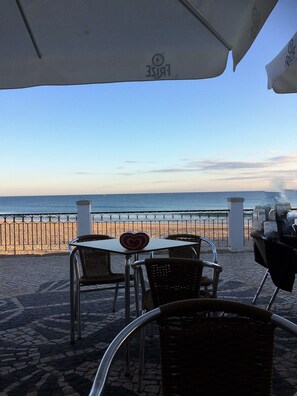 Un patio frente al mar con mesas y sillas, con vista a la playa y al océano.