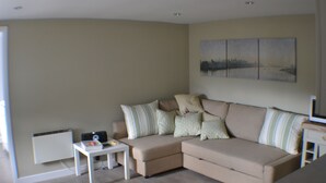 A living room with a beige sectional sofa, a small white table, and a radiator.