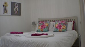 A neatly made bed with floral pillows, a folded towel, and a framed picture on the wall.