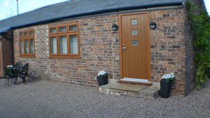 A brick building with a wooden door and windows, a gravel driveway, and outdoor furniture.