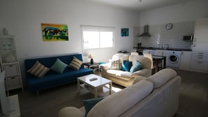 A modern living room with a blue sofa, a beige sofa, and a coffee table. There is a kitchen area with a microwave, stove, and washing machine. - Beautiful villa with garden, Jacuzzi and sea views (Arona)