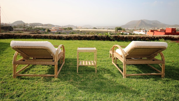 Two wicker lounge chairs with cushions on a grassy lawn, a small wooden table, and a view of distant buildings and hills. - Beautiful villa with garden, Jacuzzi and sea views (Arona)