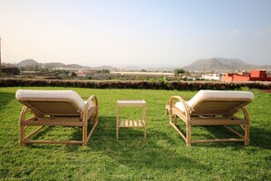 Two wicker lounge chairs with cushions on a grassy lawn, a small wooden table, and a view of distant buildings and hills. - Beautiful villa with garden, Jacuzzi and sea views (Arona)