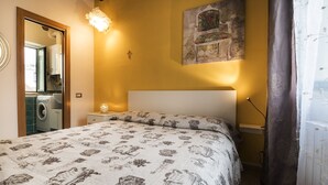 A bedroom with a bed, a nightstand, a wall-mounted lamp, a painting, and a washing machine in the corner. - Historic Center Salerno, ideal for getting around the city and the coast - Wi-Fi Free (Salerno)