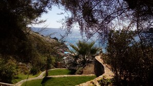 A pathway leading to a coastal area with a view of the sea, surrounded by greenery and a stone wall. - Villa Ostria, Lefkogia Cottage on a 20.000 sq.m.farm! Only 1 km from the beach.  (Rethymno)