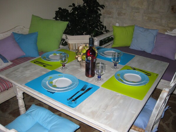 A dining table set with plates, cutlery, and wine glasses, surrounded by a sofa with cushions.