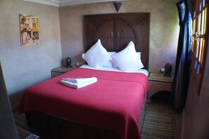 Ein Zimmer mit einem Bett, einer Holztür, einem kleinen Tisch und einem an der Wand hängenden Gemälde.