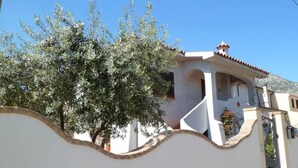 Un edificio blanco con techo de tejas, un pequeño balcón y un árbol en la fachada.