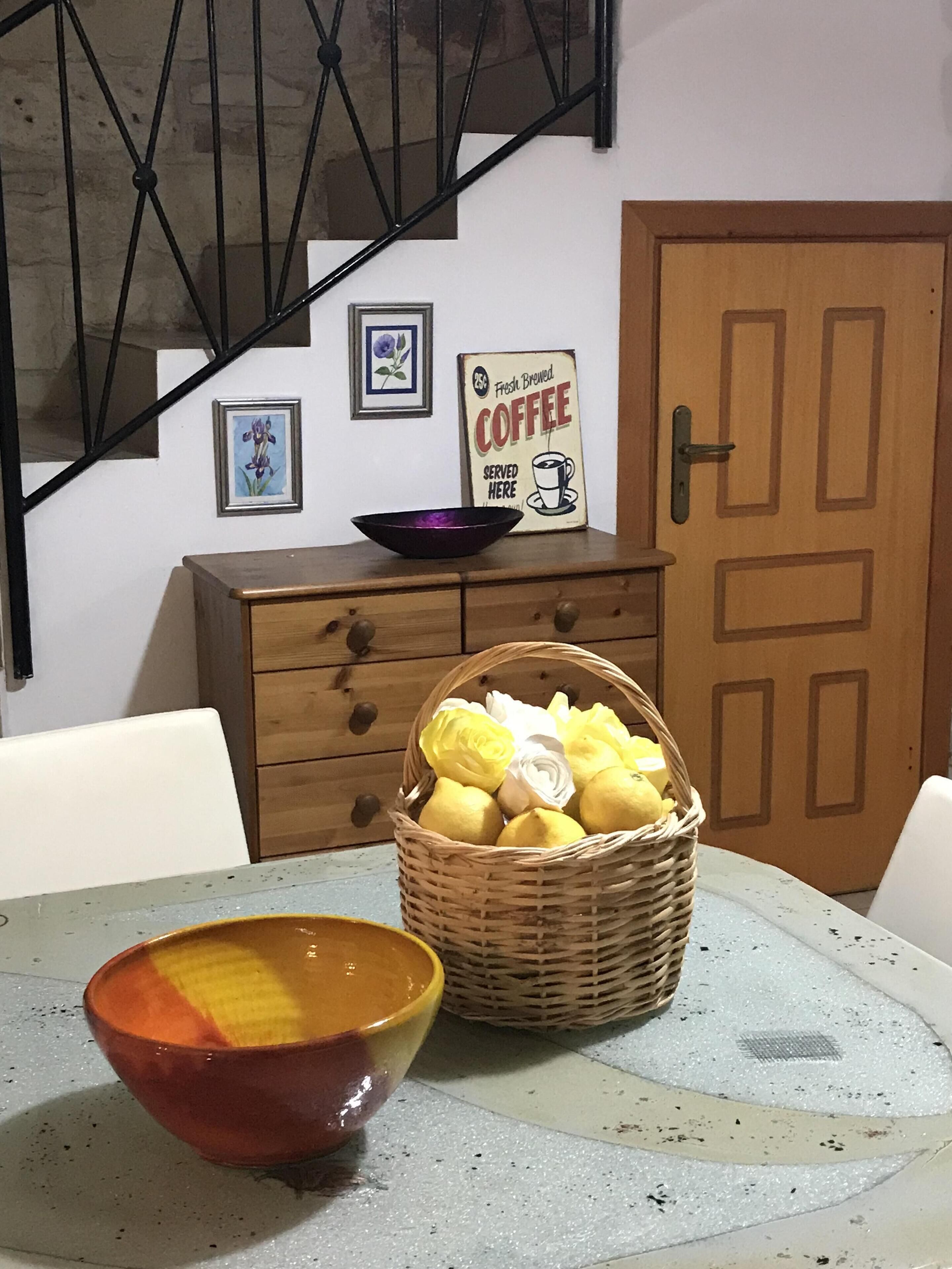 A dining table with a bowl and a basket of lemons and flowers.