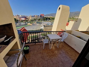 Ein Balkon mit Tisch, Stühlen, einem Grill und Blick auf ein Sportfeld sowie Gebäude im Hintergrund.