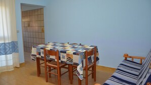 Un comedor con una mesa cubierta por un mantel estampado, sillas de madera, un sofá y una pared de azulejos.