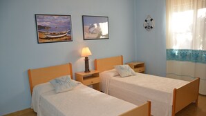 Una habitación con dos camas individuales, una mesita de noche con lámpara y dos cuadros en la pared.