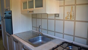 Una cocina con un lavamanos de acero inoxidable, una estufa a gas, armarios de madera y un salpicadero de azulejos.