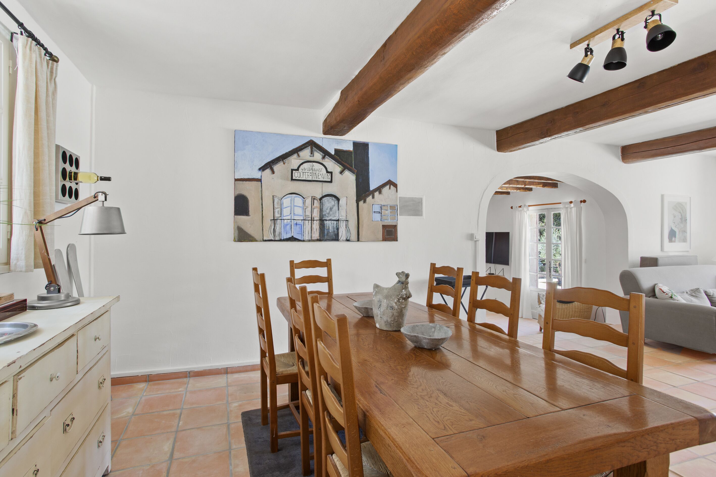 A dining area with a wooden table, chairs, and a painting of a building on the wall.