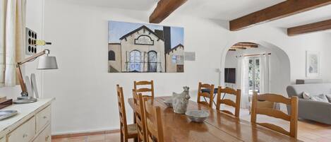 A dining area with a wooden table, chairs, and a painting of a building on the wall.