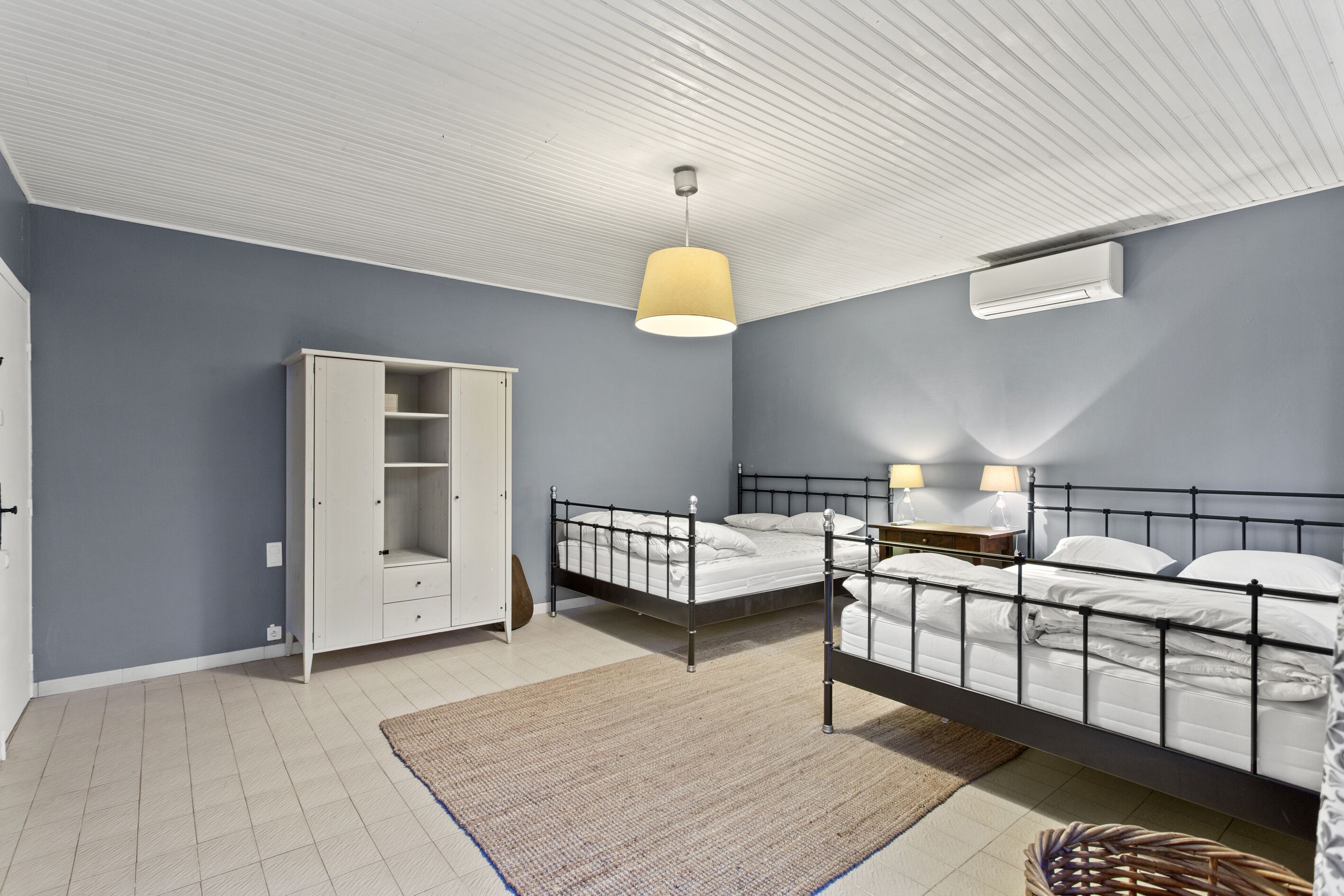 A bedroom with two beds, a wardrobe, a ceiling fan, and an air conditioning unit.