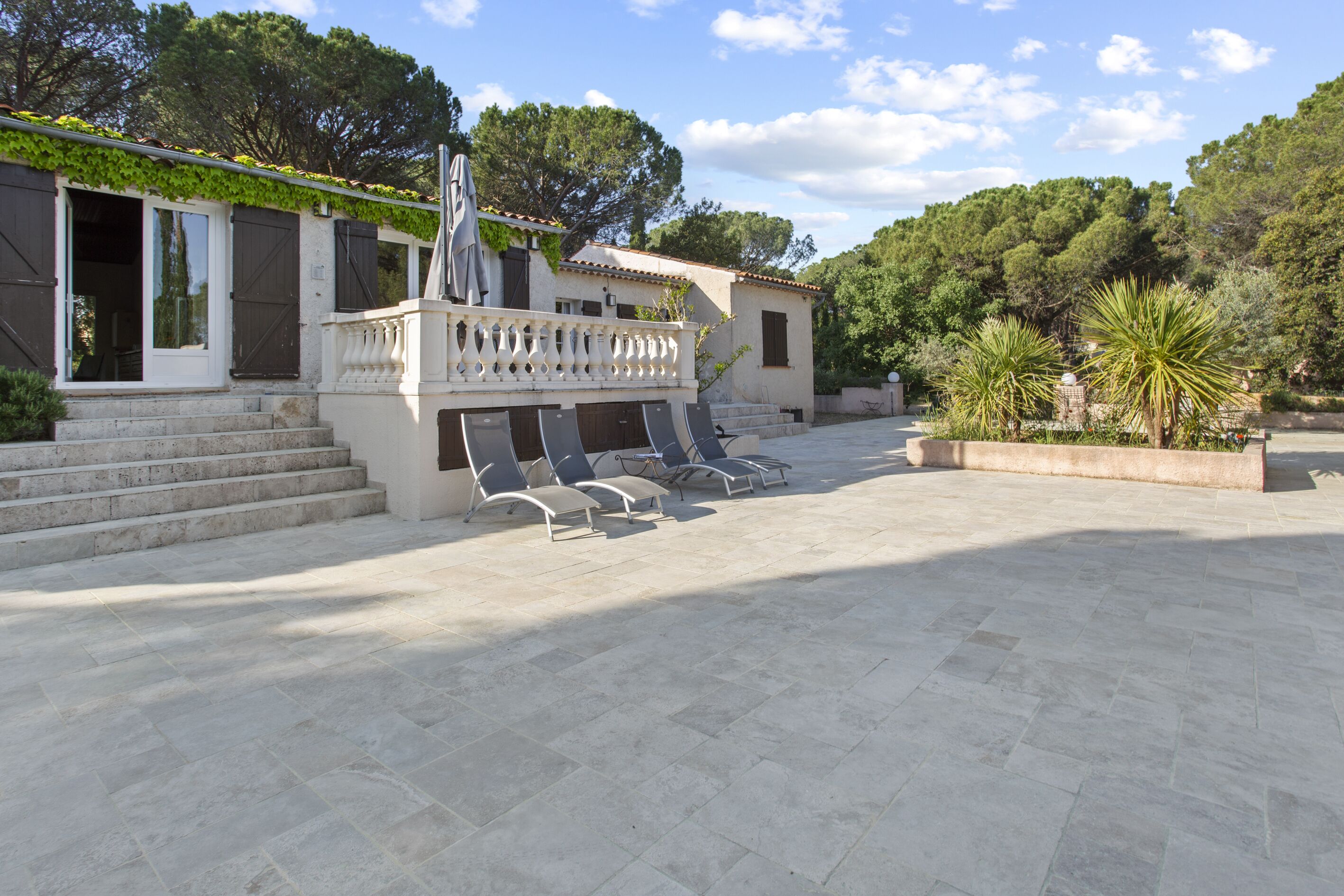 A courtyard with stone flooring, outdoor seating, and a building with a balcony.
