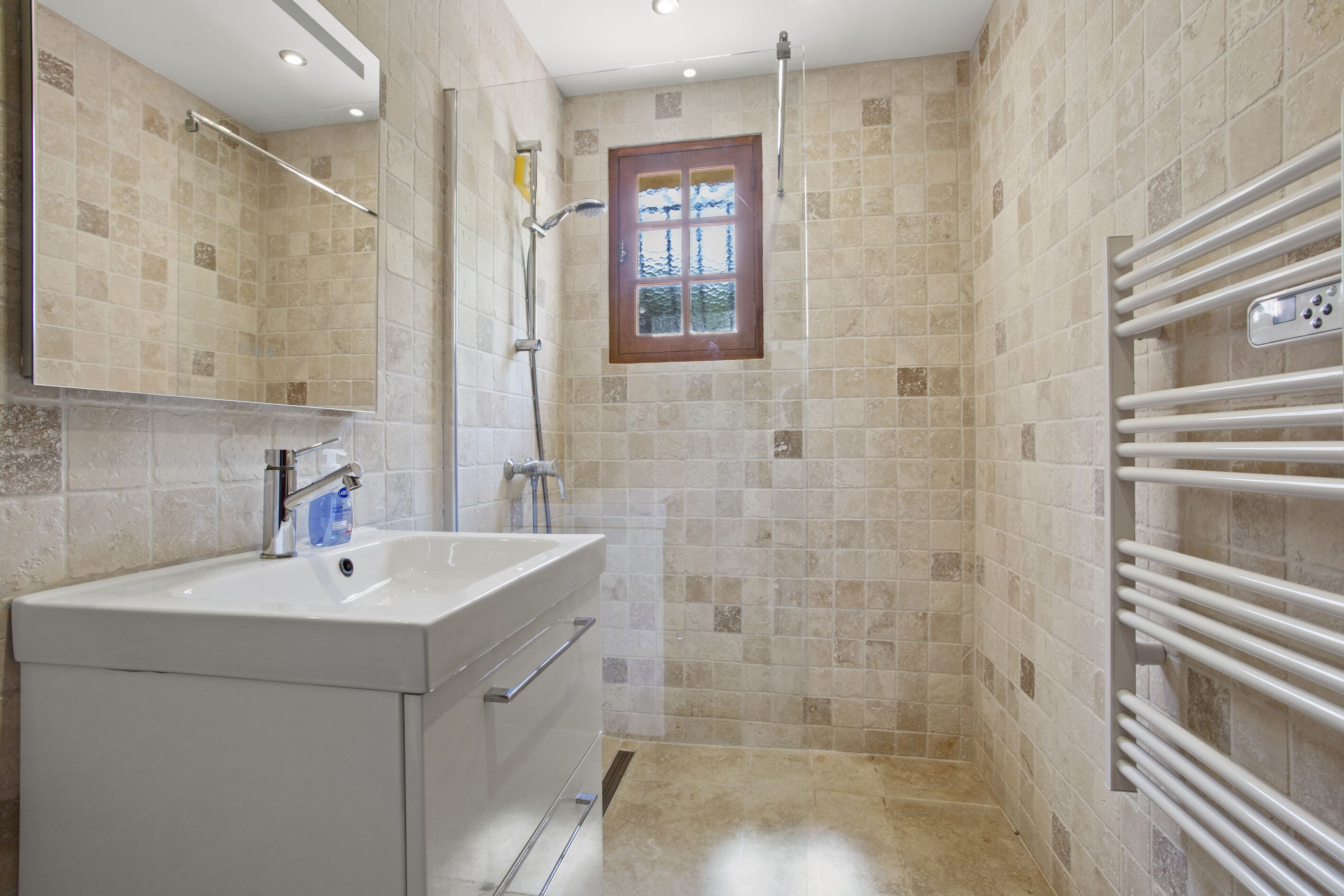 A bathroom with a sink, mirror, shower, and a window.