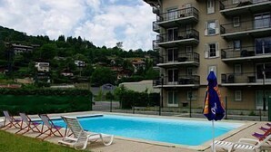 A swimming pool with lounge chairs and a blue umbrella, surrounded by a building with balconies. - Winter/Summer holidays in St Gervais Le Bains Sleeps 4 (Saint-Gervais-Les-Bains)