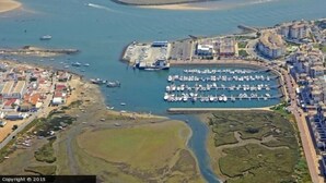 An aerial view of a coastal marina with boats docked, a parking area, and residential buildings. - Luxury beach penthouse apartment in ISLA CANELA. The best views front line beach (URBANIZACION LOS CISNES)