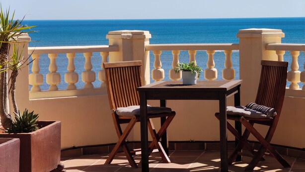 A balcony with a view of the sea, two wooden chairs, a small table, and potted plants. - Luxury beach penthouse apartment in ISLA CANELA. The best views front line beach (URBANIZACION LOS CISNES)