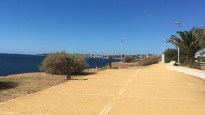 Un sendero arenoso que conduce a una playa, con vista despejada al mar y un paisaje urbano lejano.