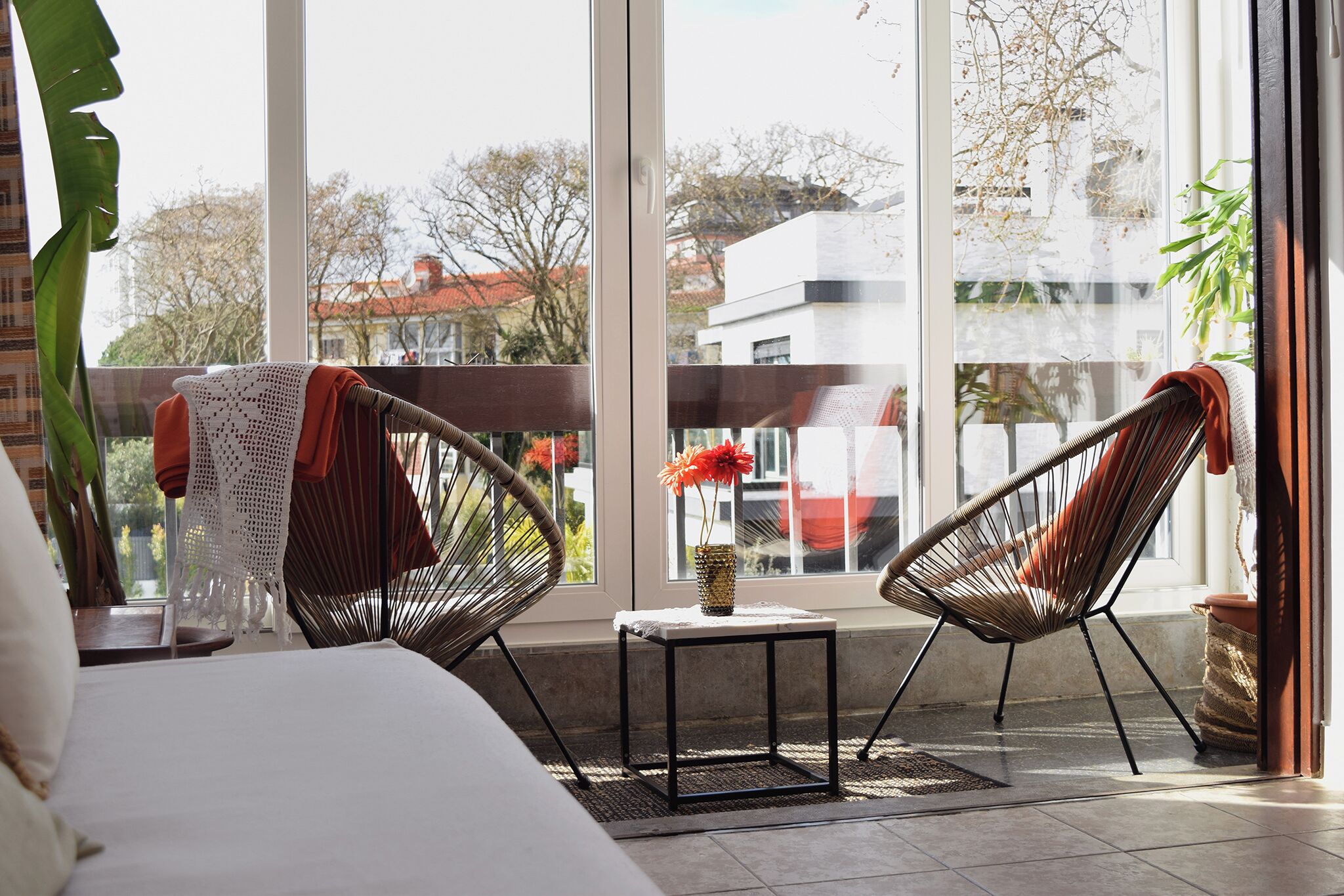 Ein Balkon mit Korbstühlen, einem kleinen Tisch und einer Blumenvase.