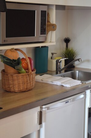 A kitchen with a microwave, a sink, a dishwasher, and a basket of vegetables on the counter.