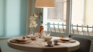 A dining table set with white dishes, glasses, and a bottle, with a view of a balcony and a railing.
