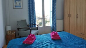 Ein Zimmer mit einem Bett, einem Sessel, einem Kleiderschrank und einem Fenster mit Vorhängen.