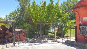 Une entrée fermée par un portail, avec une structure en bois, une pile de bûches et un portail en métal.