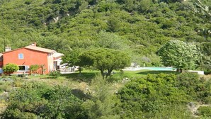 Une villa rouge dotée d’une piscine, entourée d’une végétation luxuriante et de collines.