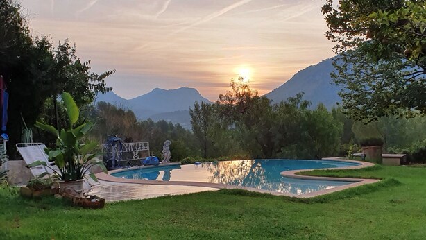 Une piscine entourée d’une pelouse et d’arbres, avec des montagnes en arrière-plan.