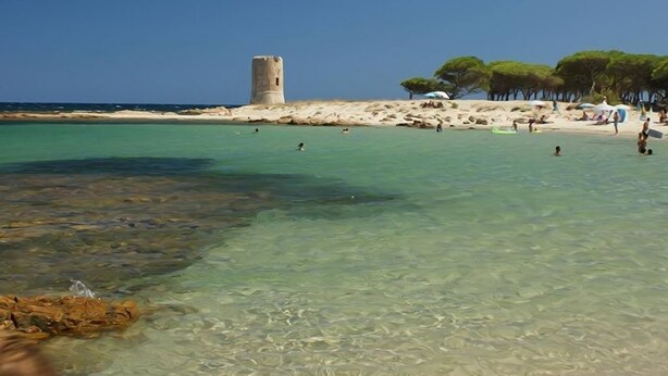 A beach with clear turquoise water, a sandy shore, and a tower structure. - Peaceful Holiday Home. (Posada)