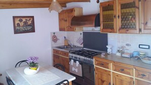 A kitchen with wooden cabinets, a gas stove, a sink, and a dining area with a table and chairs. - Peaceful Holiday Home. (Posada)