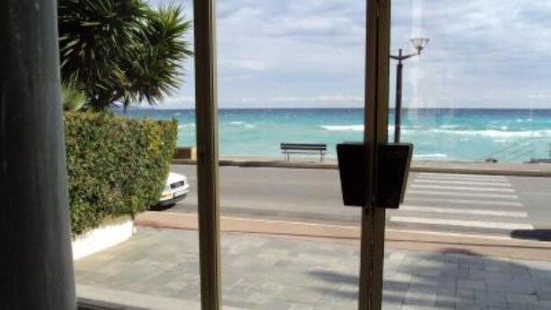 Vue depuis l’intérieur d’un bâtiment doté de grandes fenêtres donnant sur une plage et l’océan.